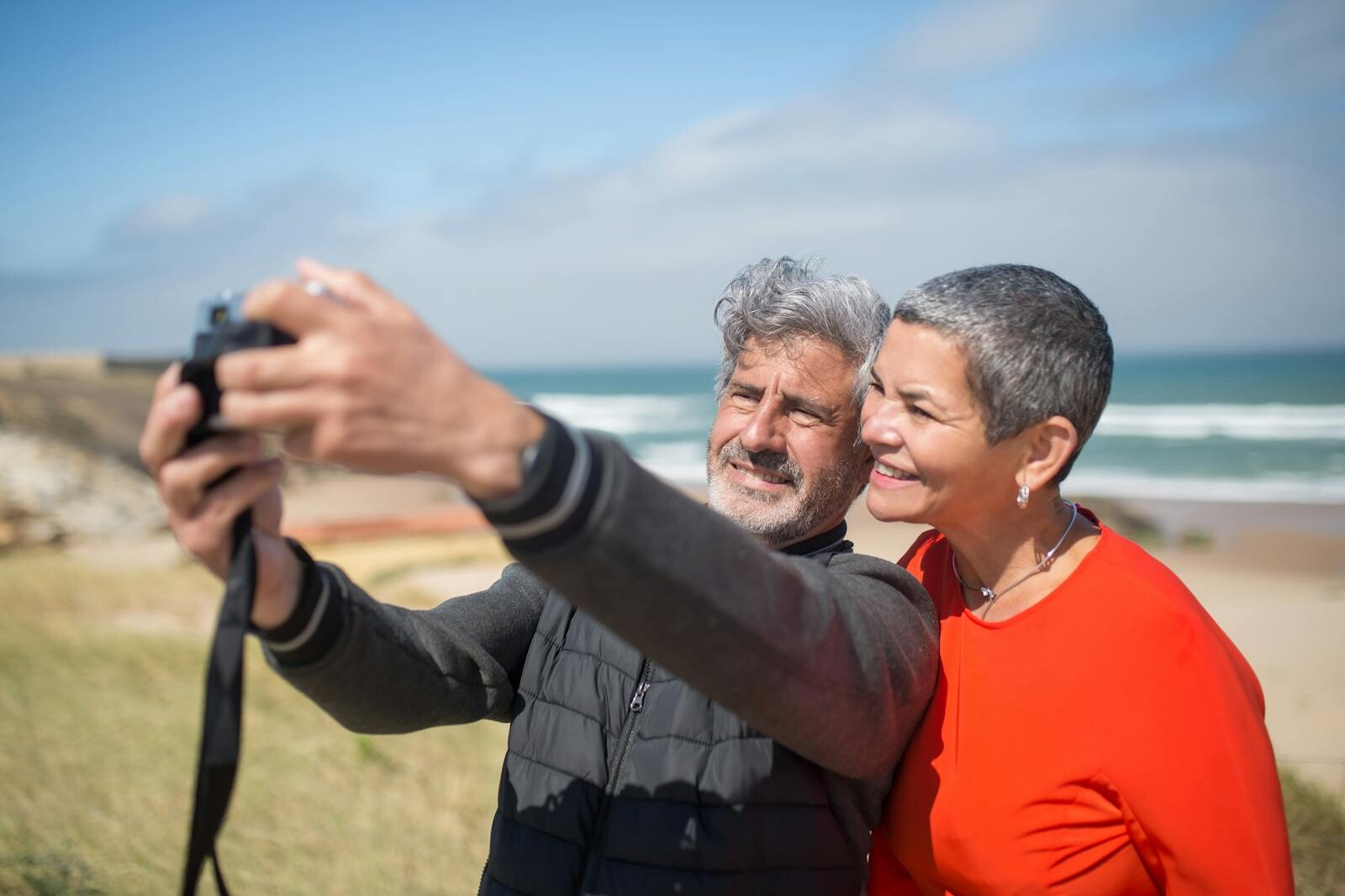 Happy elderly couple capturing a selfie on a scenic beach in Portugal. Lifestyle moment.