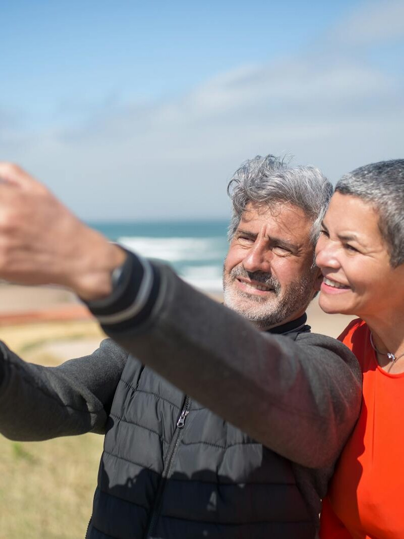 Happy elderly couple capturing a selfie on a scenic beach in Portugal. Lifestyle moment.