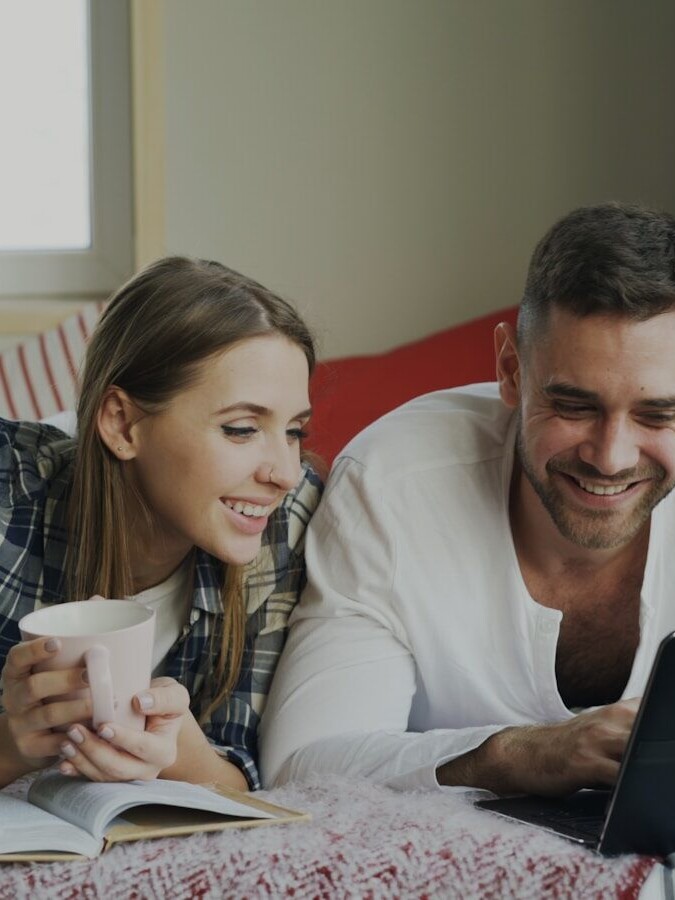 Couple lying on bed with laptop and coffee
