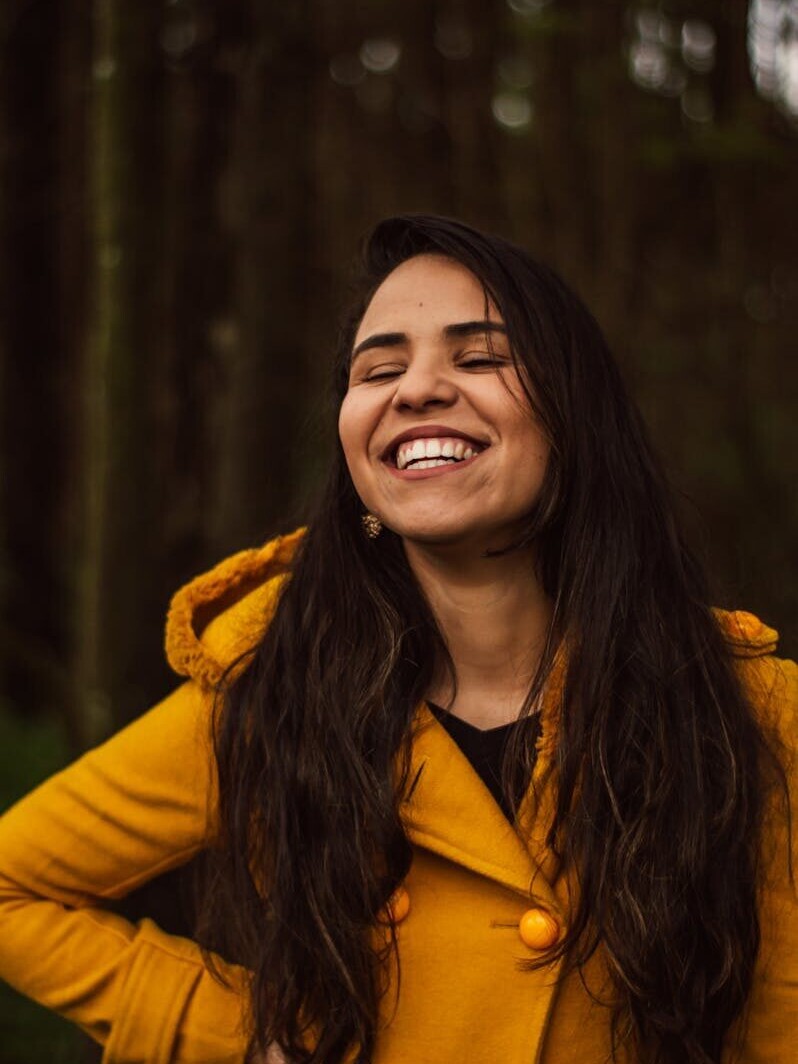 A smiling woman in a yellow coat enjoying a cheerful moment outdoors in São Paulo.
