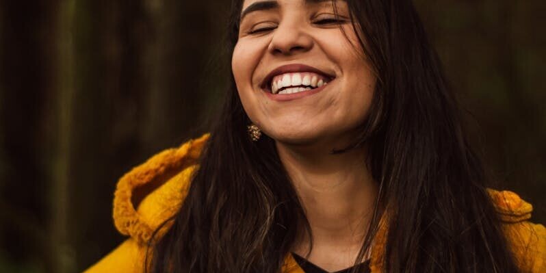 A smiling woman in a yellow coat enjoying a cheerful moment outdoors in São Paulo.