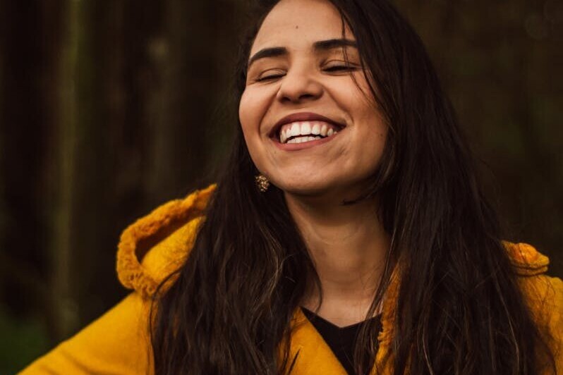 A smiling woman in a yellow coat enjoying a cheerful moment outdoors in São Paulo.