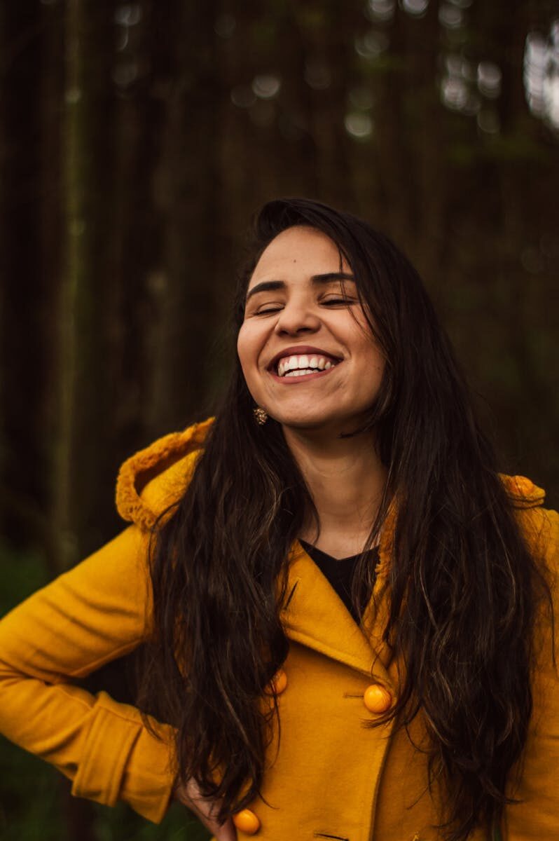 A smiling woman in a yellow coat enjoying a cheerful moment outdoors in São Paulo.