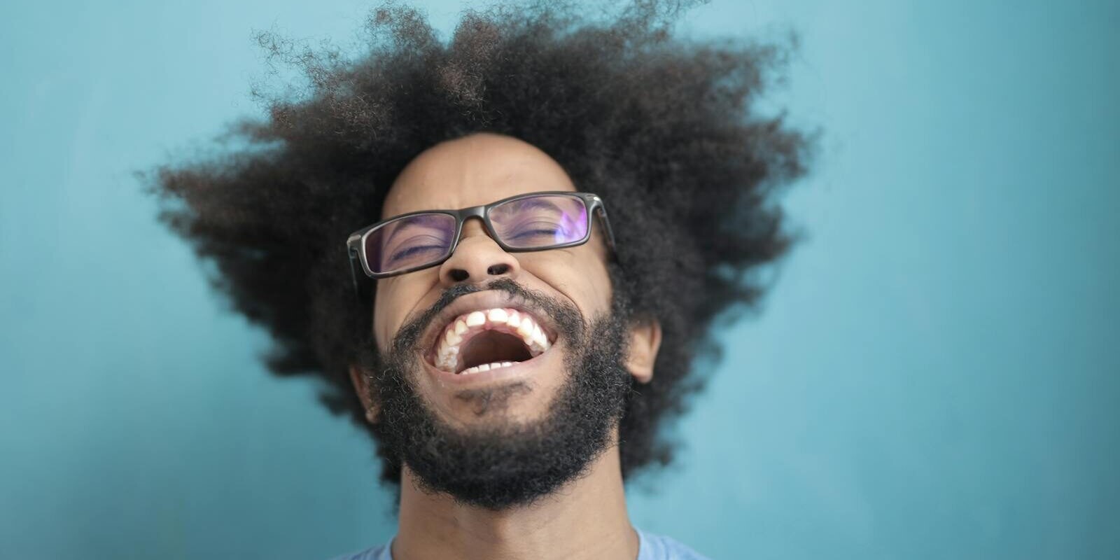 Portrait of a joyful man laughing with an afro hairstyle against a blue background.
