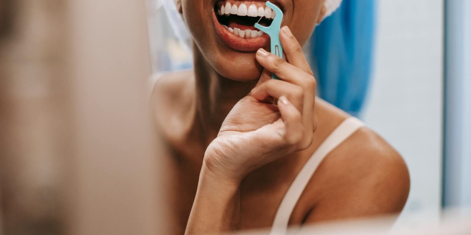 Young African American woman practicing oral hygiene by flossing teeth in front of a bathroom mirror.