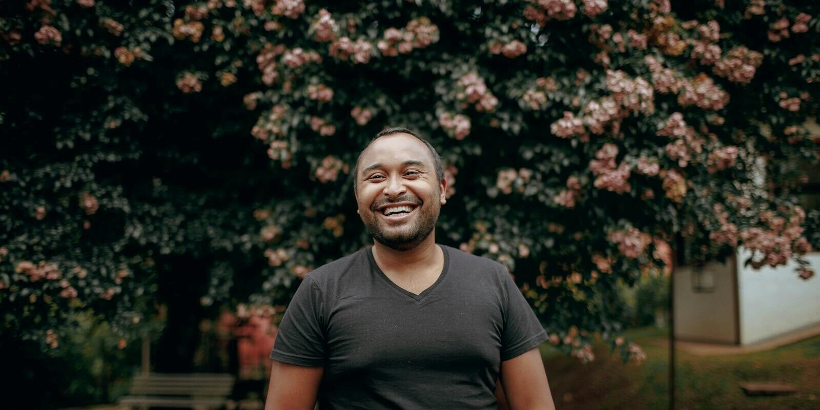 Cheerful man standing in park, vibrant blooming tree behind him.