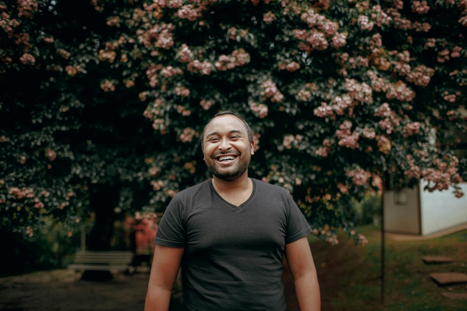 Cheerful man standing in park, vibrant blooming tree behind him.