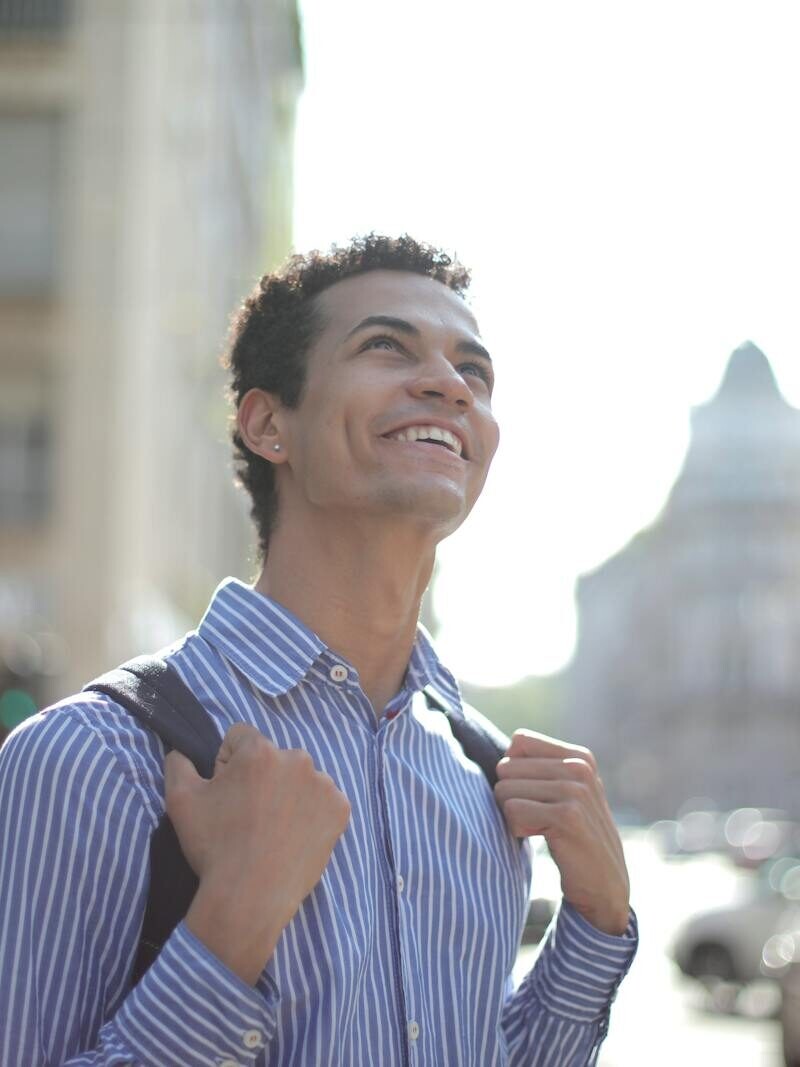 A joyful young man in a striped shirt enjoys a sunny day in the city, radiating happiness.