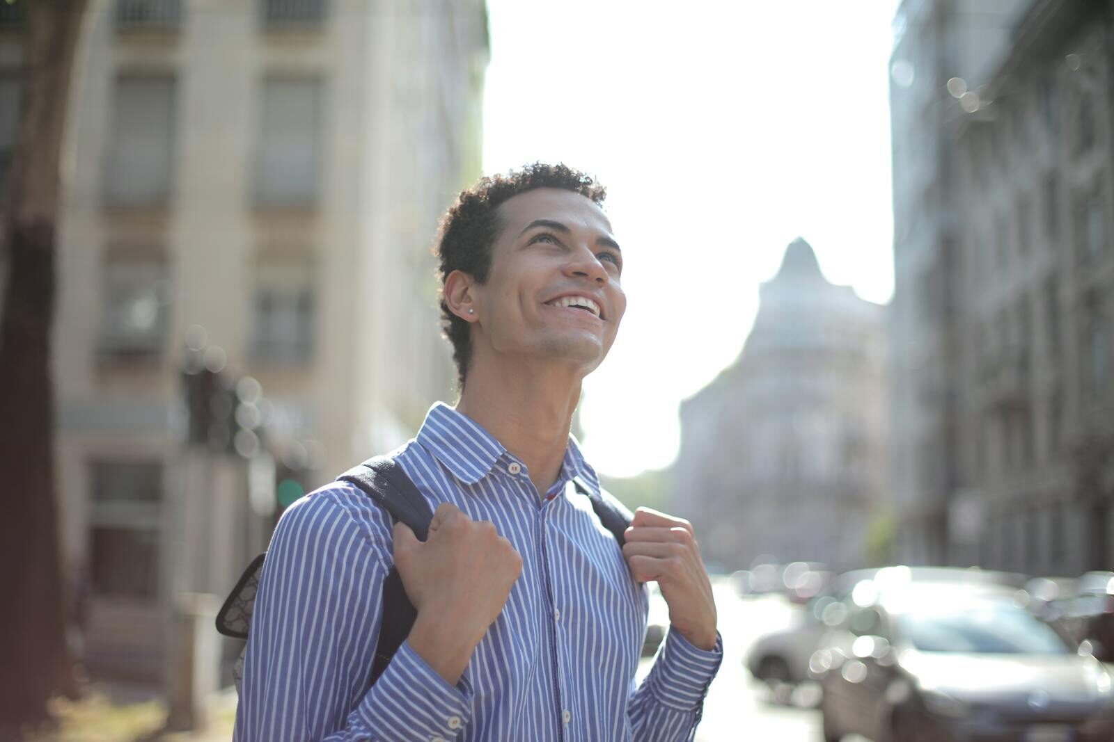 A joyful young man in a striped shirt enjoys a sunny day in the city, radiating happiness.