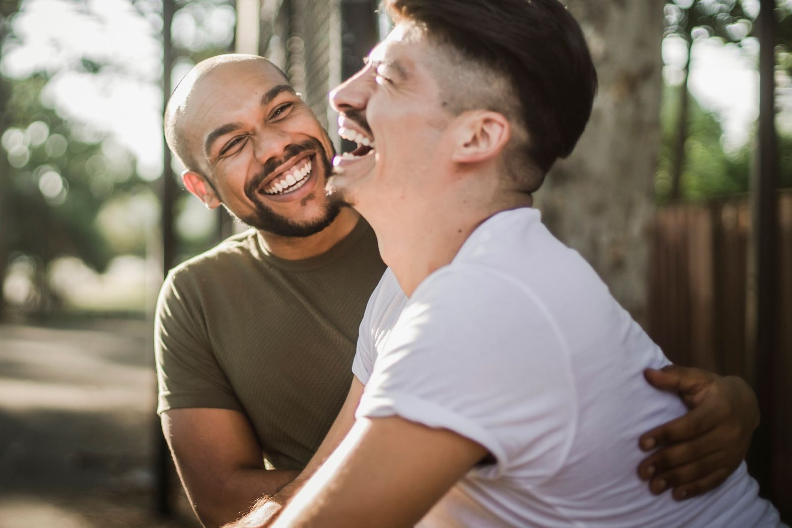 Happy interracial gay couple laughing and embracing outdoors, showcasing love and happiness.