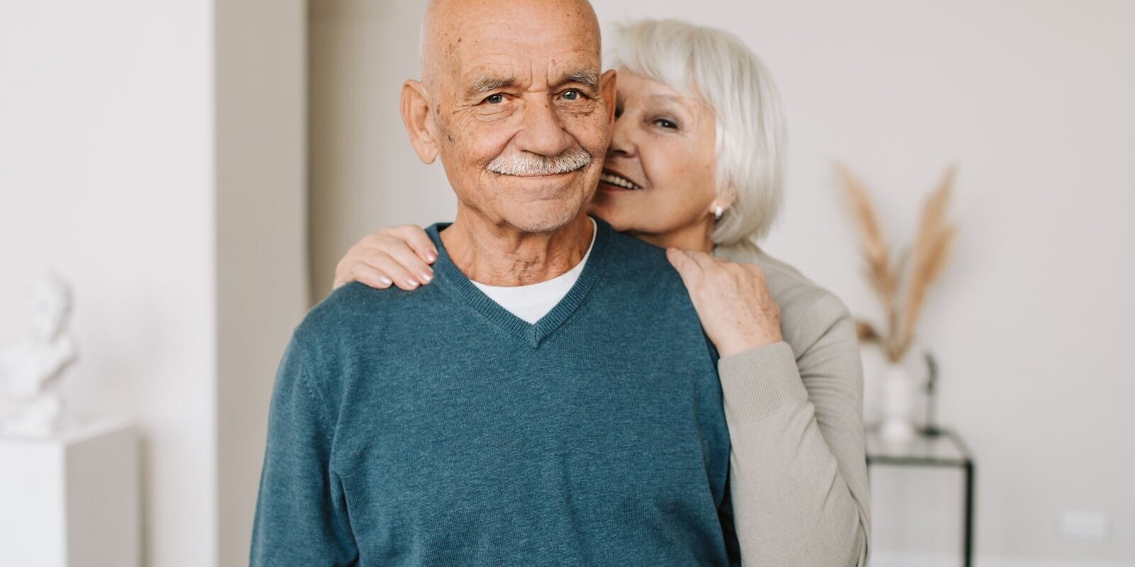 A joyful elderly couple embracing each other in a cozy indoor setting, exuding love and happiness.