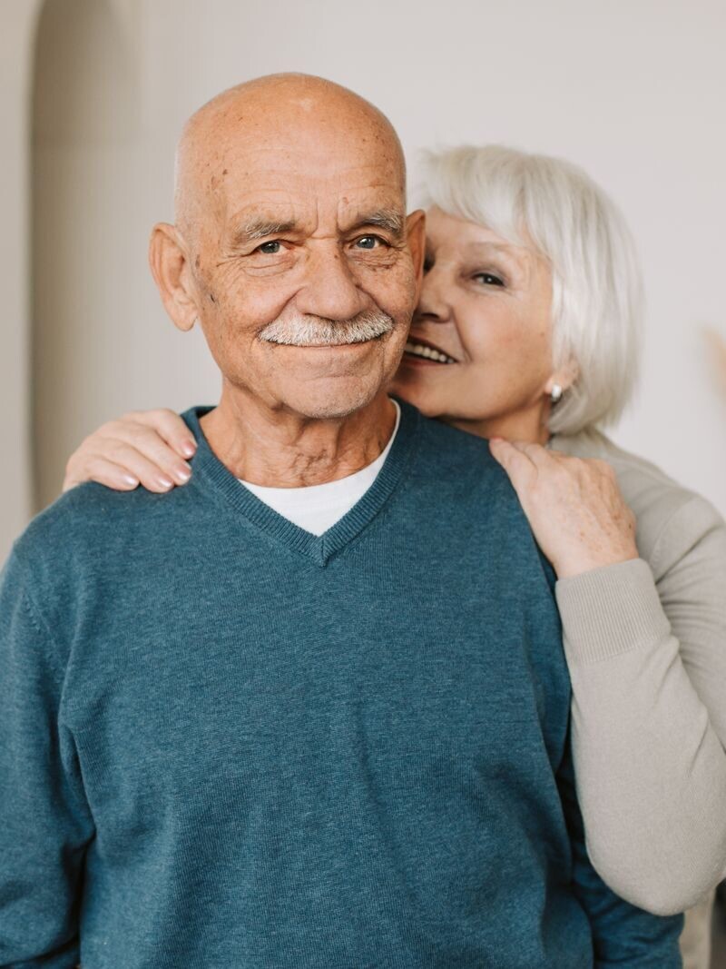 A joyful elderly couple embracing each other in a cozy indoor setting, exuding love and happiness.