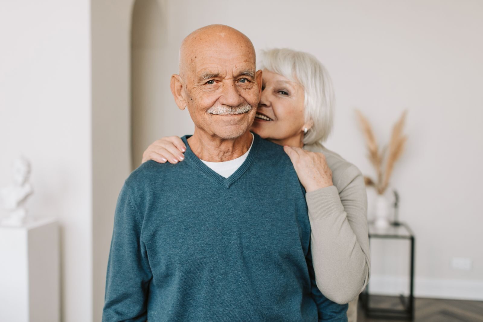 A joyful elderly couple embracing each other in a cozy indoor setting, exuding love and happiness.