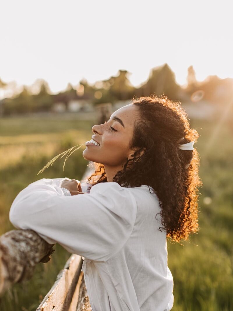 Portrait of a woman in white blouse delighting in a sunny outdoor sunset, leaning on a fence.