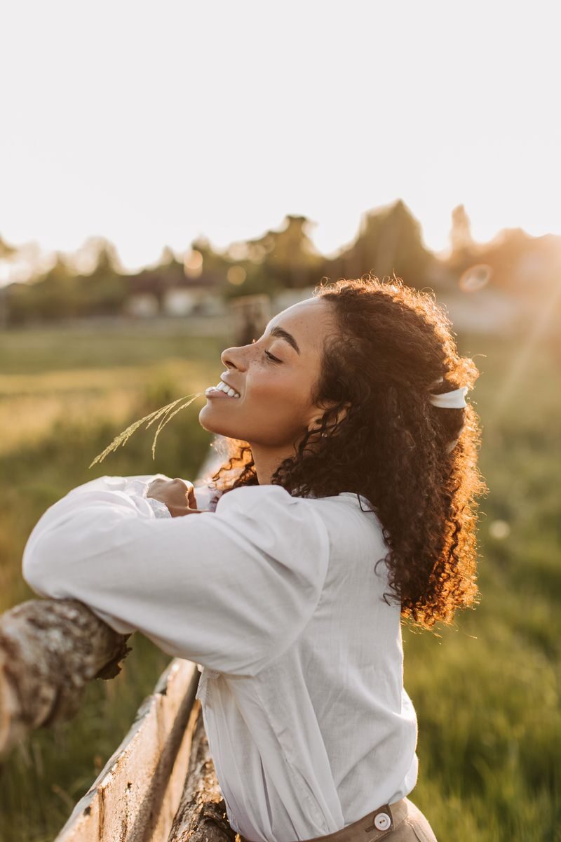 Portrait of a woman in white blouse delighting in a sunny outdoor sunset, leaning on a fence.